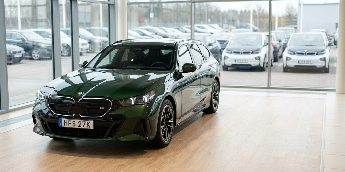 Ny grön BMW i5 touring i bilhallen med raden av begagnade elbilar utanför glasväggen