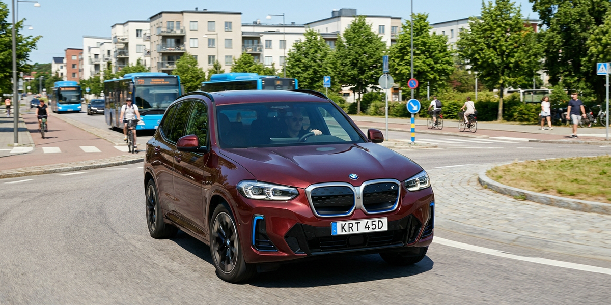 Vinröd BMW iX3 G08 i stadstrafik vid en rondell en sommardag