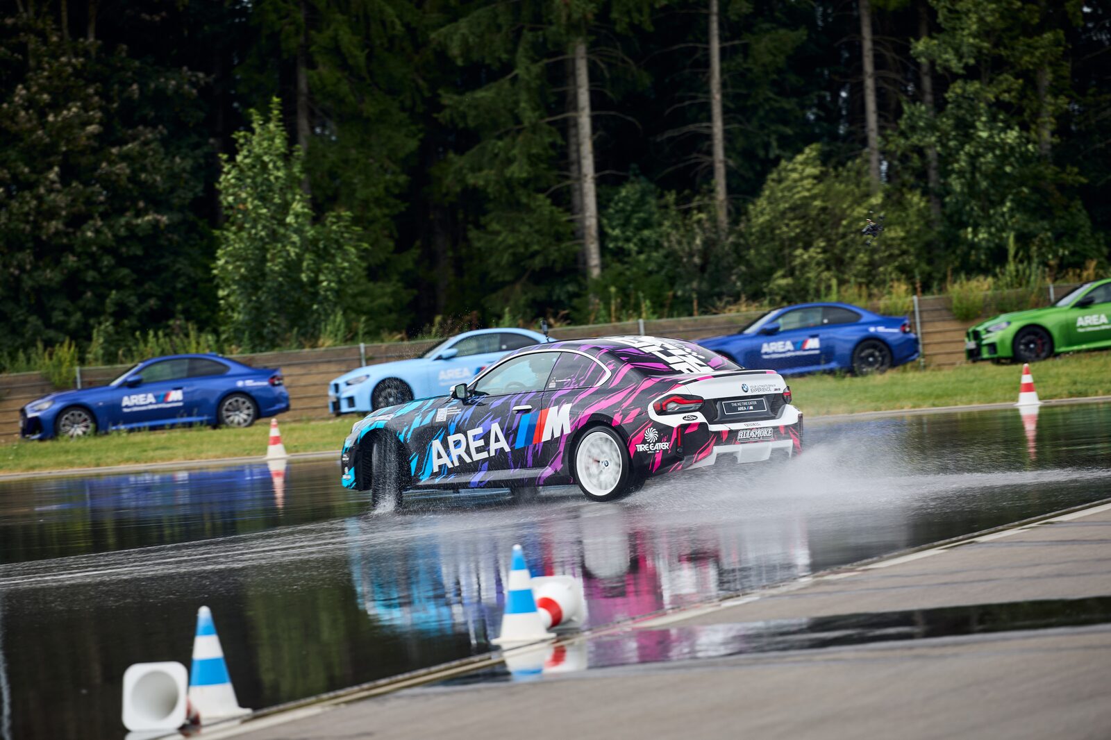 Randig BMW M2 Drift Signature i AREA M-dekor driftar förbi uppställda M2:or
