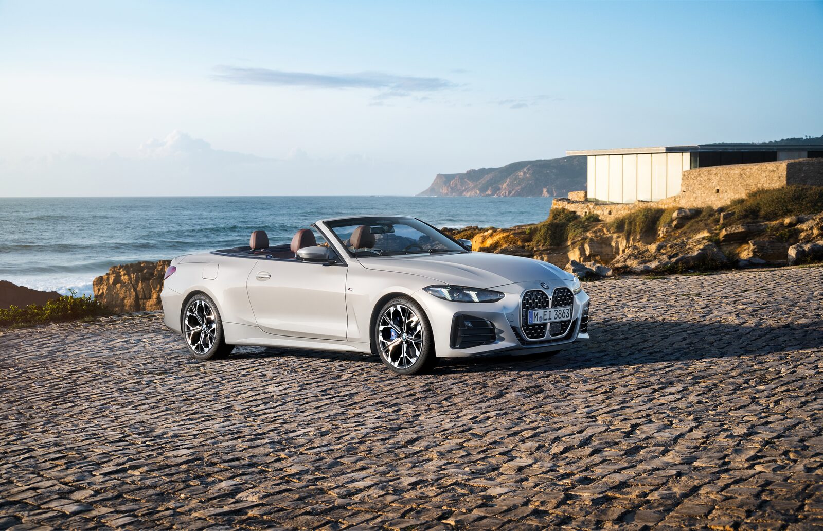 Vit BMW 4-serie Cabriolet med nedfällt suffletttak parkerad vid havet