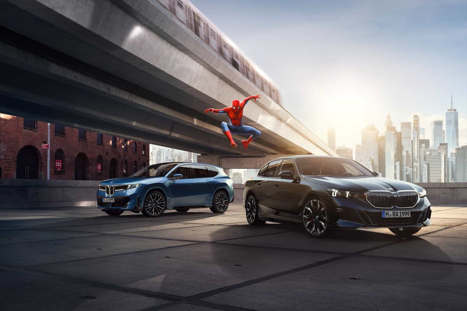 Blå BMW iX3 och svart BMW 5-serie under en tunnelbanebro i New York med Spider-Man i luften