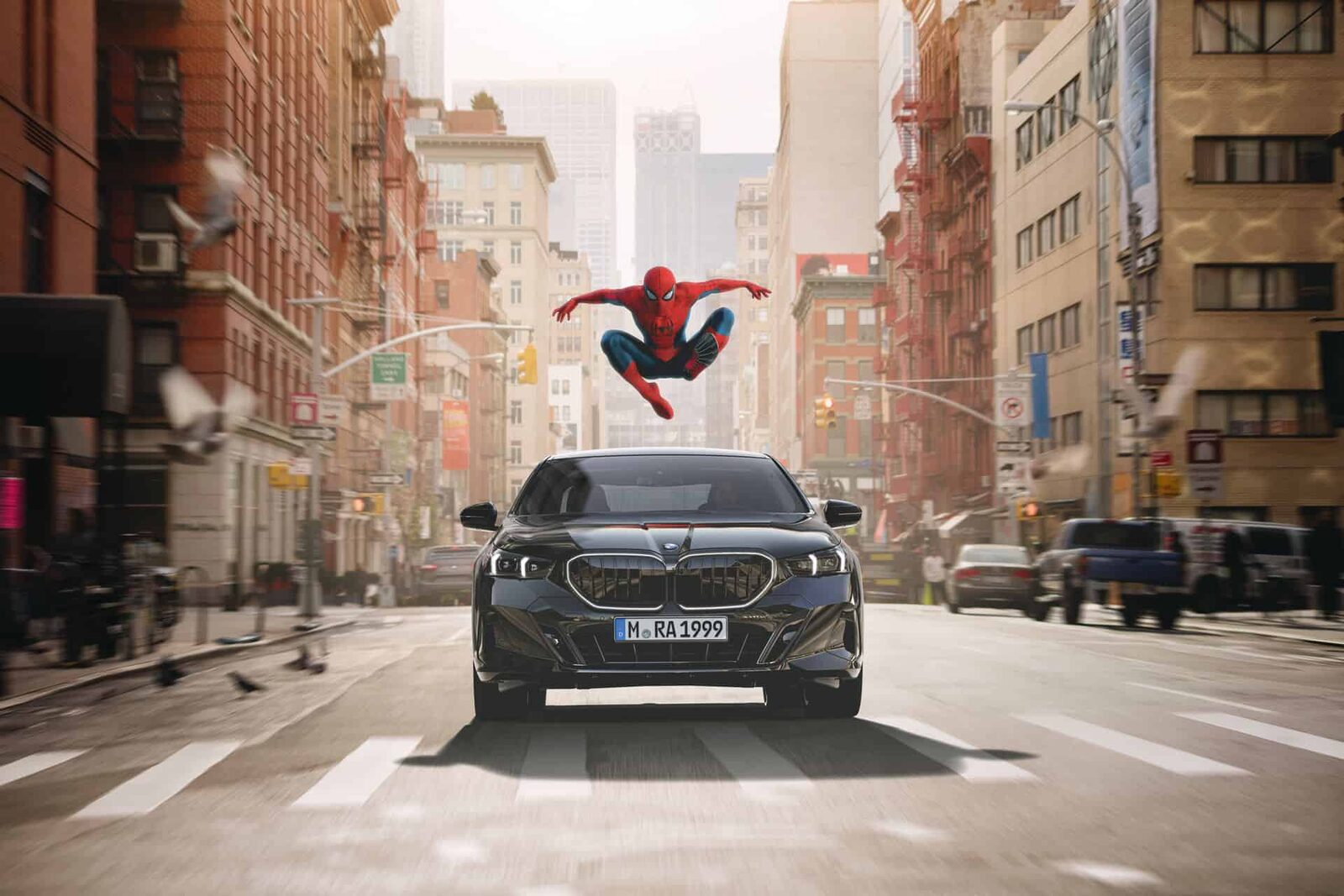 Svart BMW 5-serie framifrån på en gata i New York med Spider-Man i ett hopp ovanför bilen