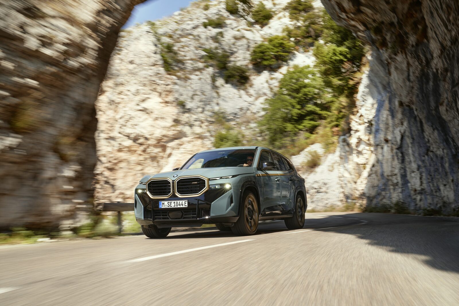 BMW XM i grönt kör på en bergsväg genom en klippformation