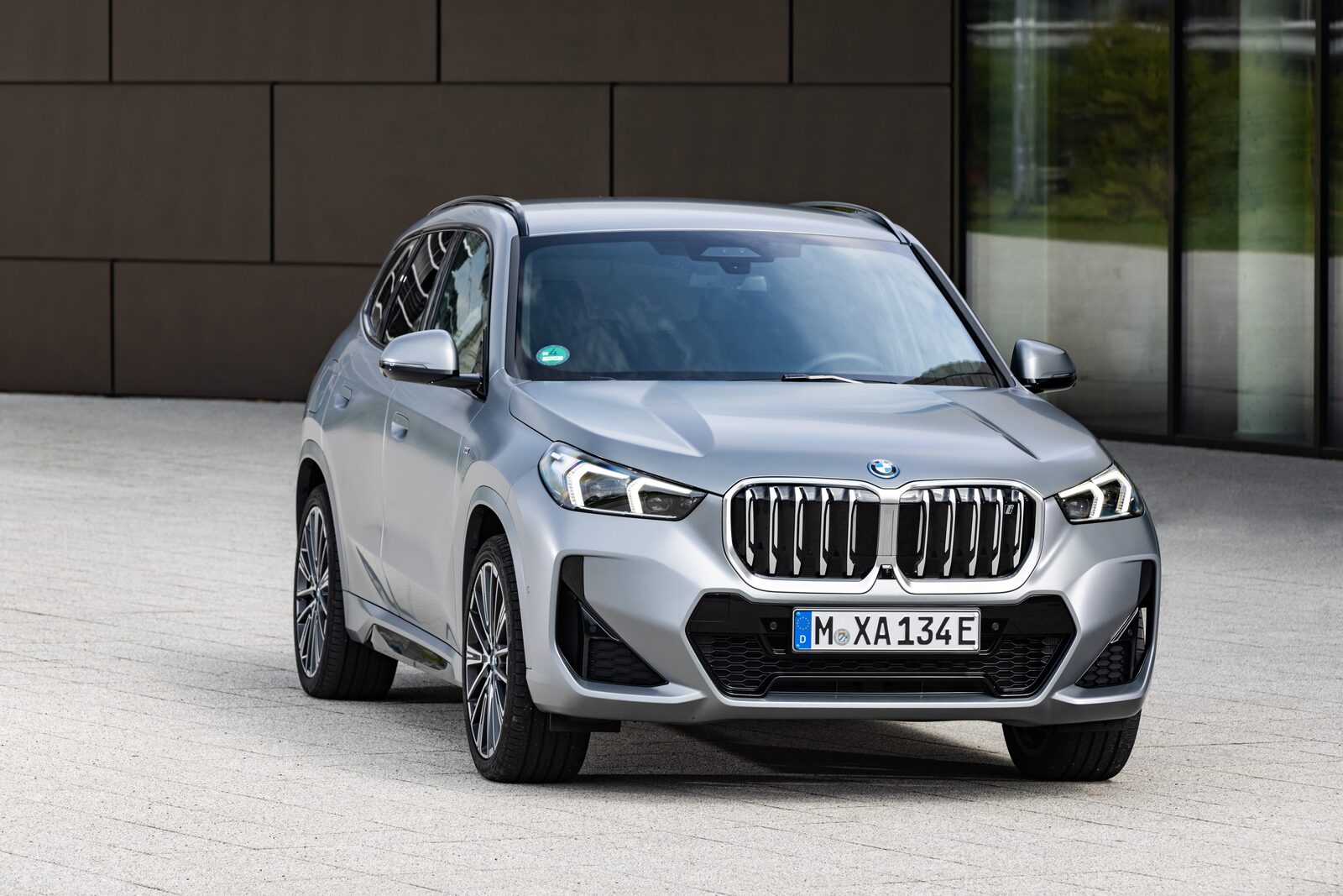 Silverfärgad BMW iX1 i trekvartsvy framifrån framför en mörk fasad