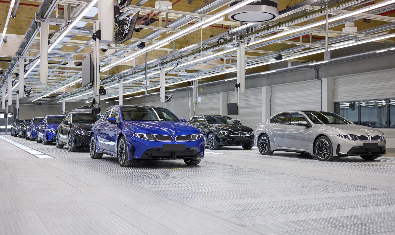 Rad av nya BMW i3 i blått, svart, grått och vitt uppställda i monteringshallen