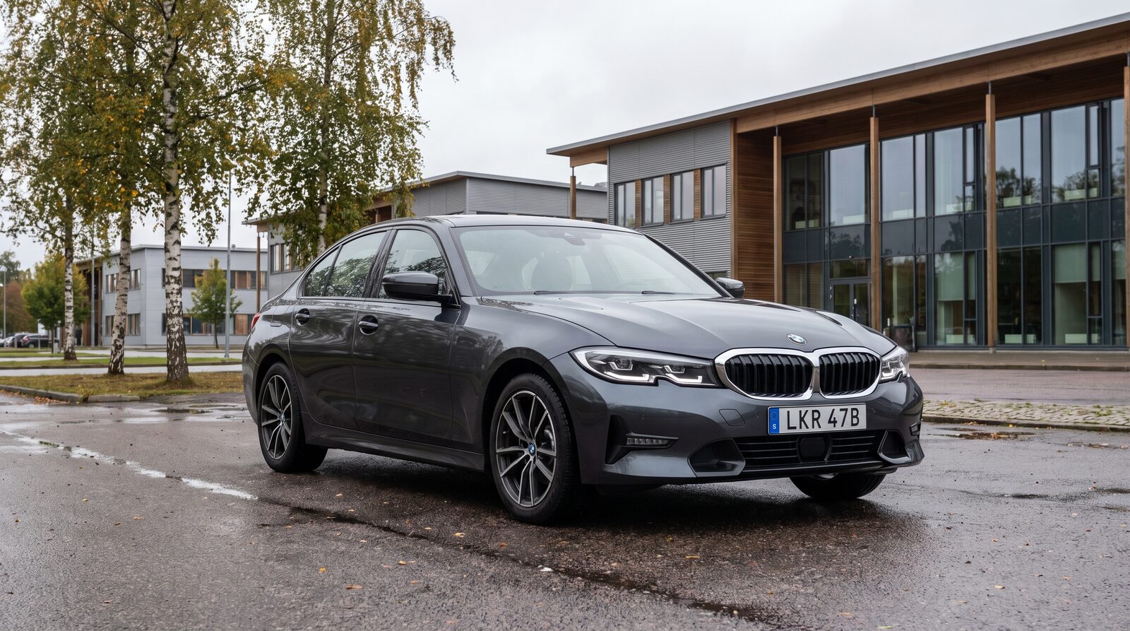 Grå BMW 3-serie sedan parkerad vid ett svenskt kontorsområde en regnig sensommardag