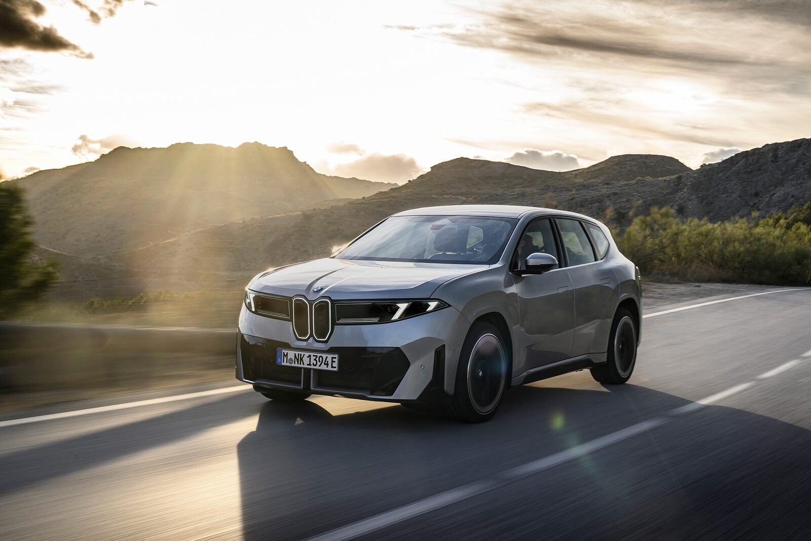 BMW iX3 i silver på landsväg i motljus mot uppgående sol