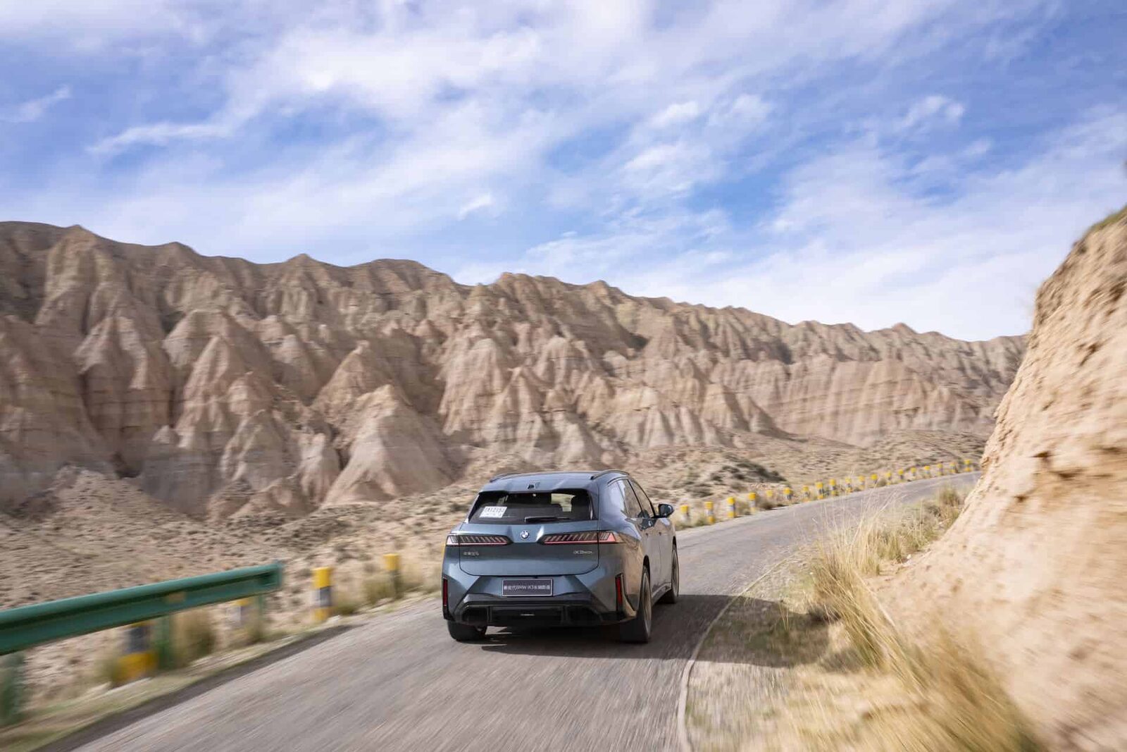 BMW iX3 bakifrån på slingrande väg genom karg bergsterräng