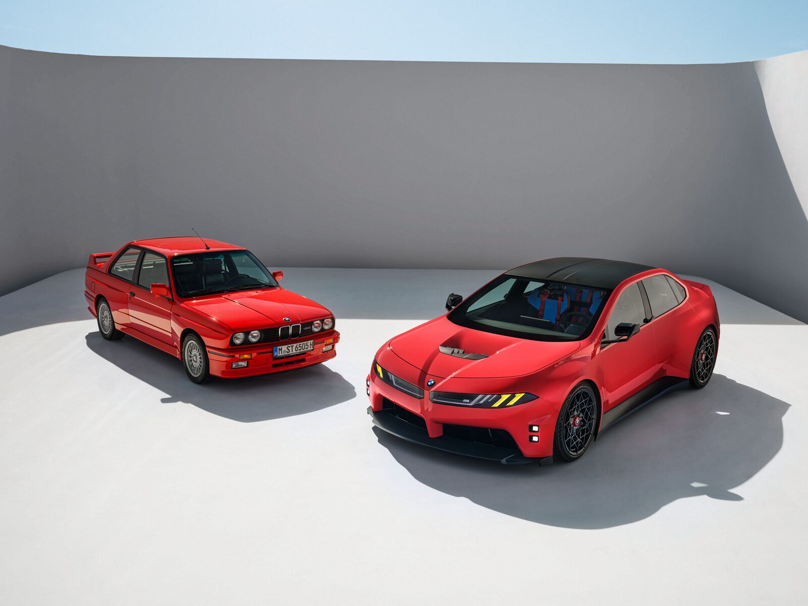 BMW M Concept Neue Klasse i rött bredvid en röd BMW M3 E30 i en studio