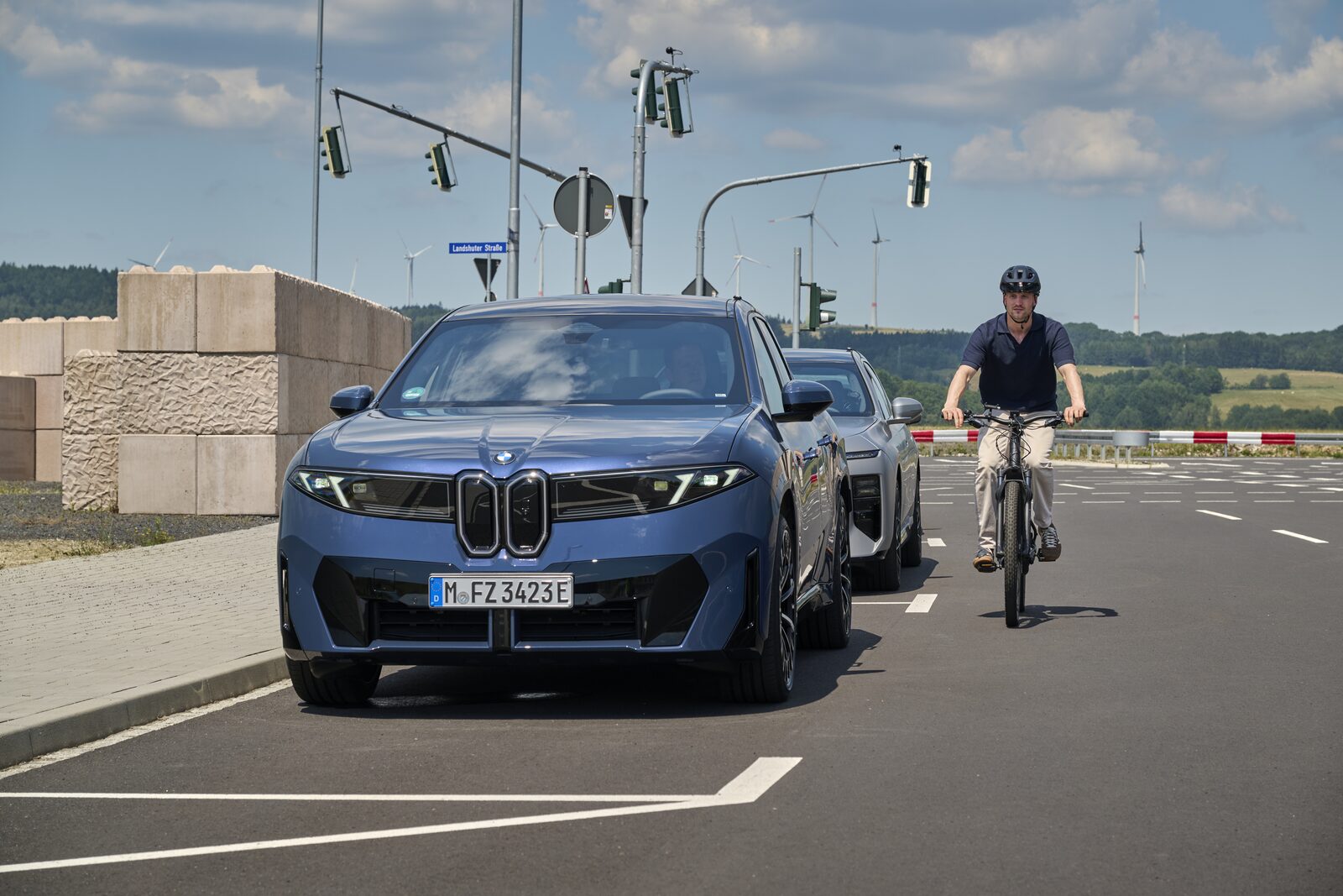 BMW iX3 står i en korsning medan en cyklist passerar framför bilen på BMW:s testanläggning