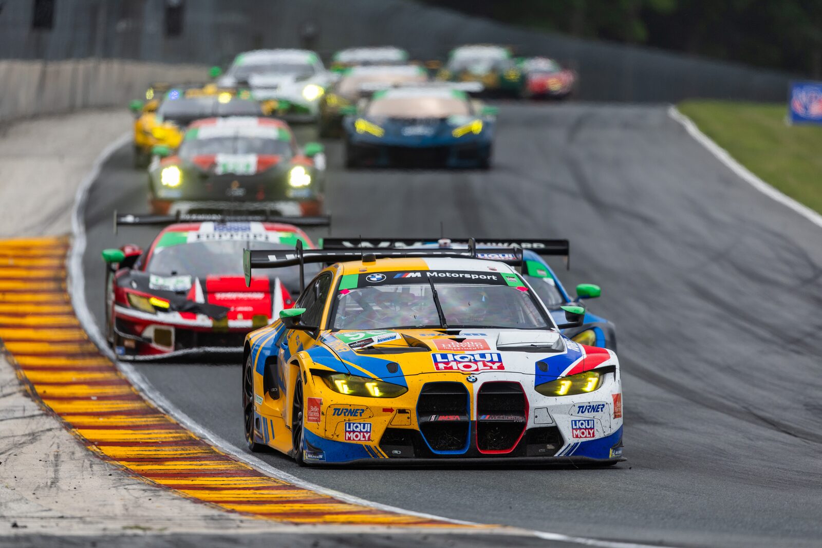 Blågul BMW M4 GT3 leder en grupp GT-bilar genom en kurva på Road America
