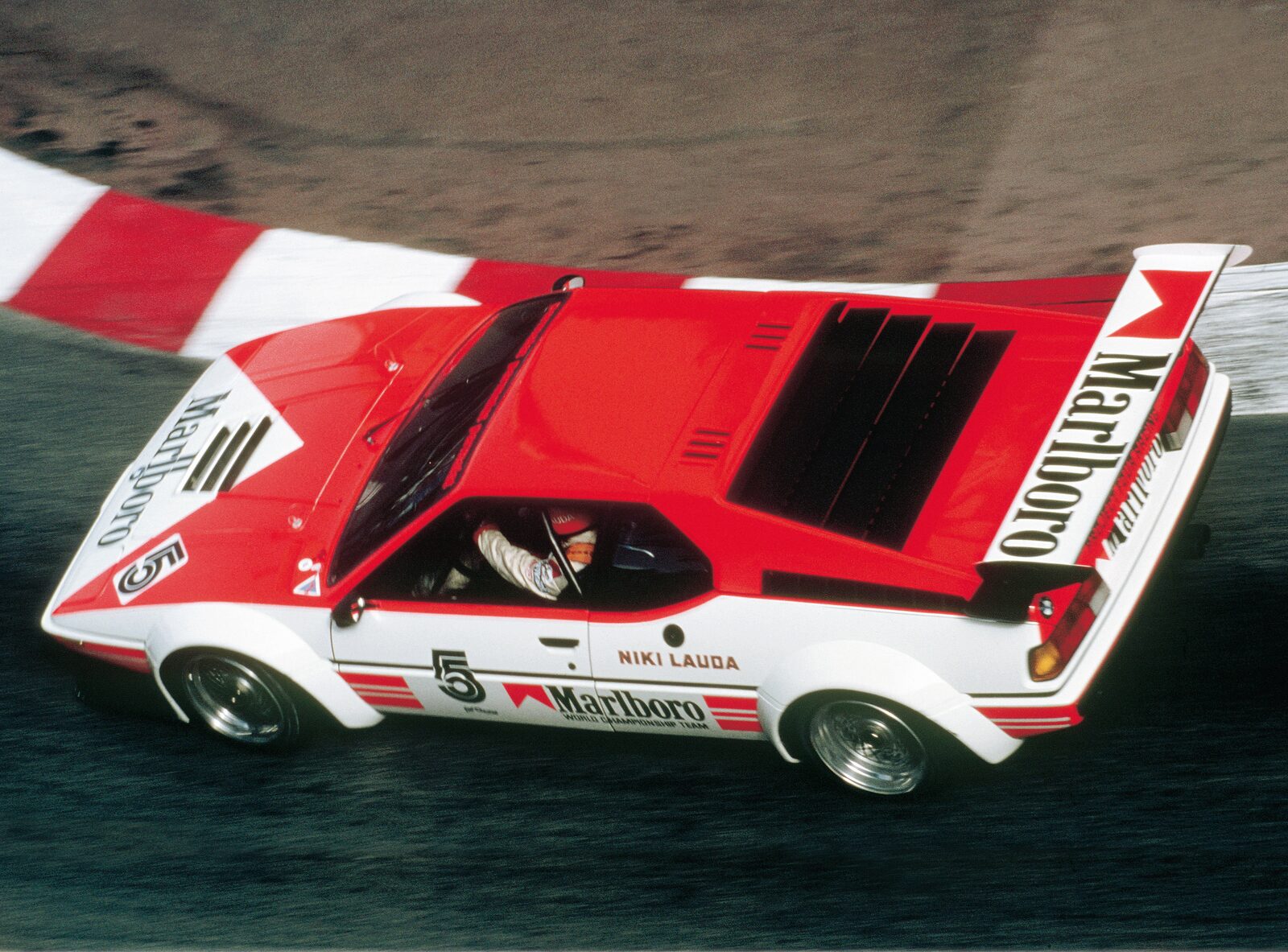 Röd BMW M1 Procar sedd snett bakifrån med stor bakvinge och breda skärmar på bana