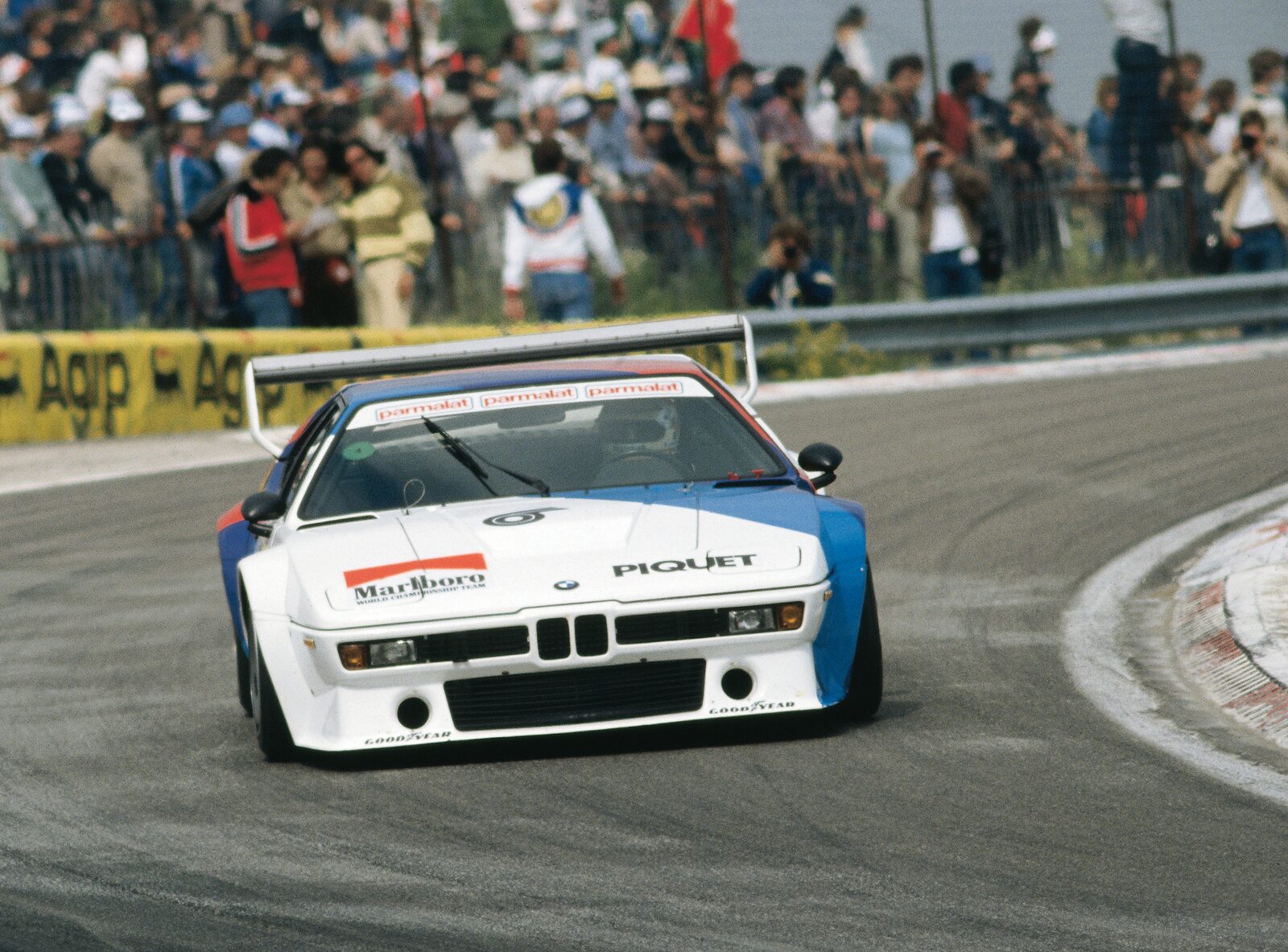 Vit BMW M1 Procar med BMW Motorsports blå och röda ränder i en kurva under lopp