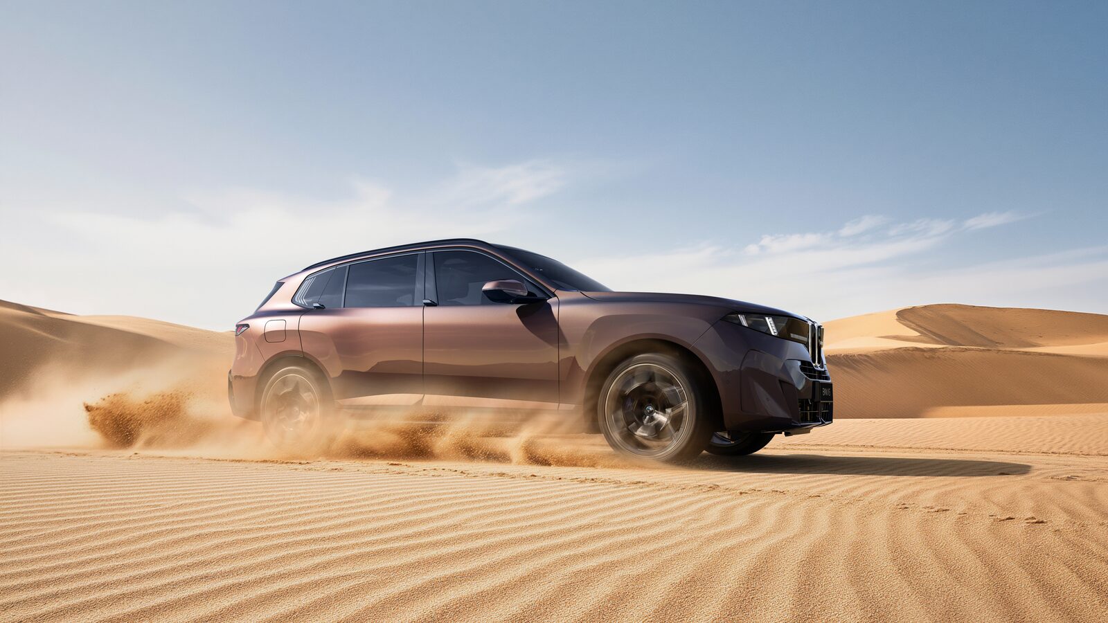 Kopparfärgad BMW X5 i fart genom öken med sand som virvlar bakom bakhjulen