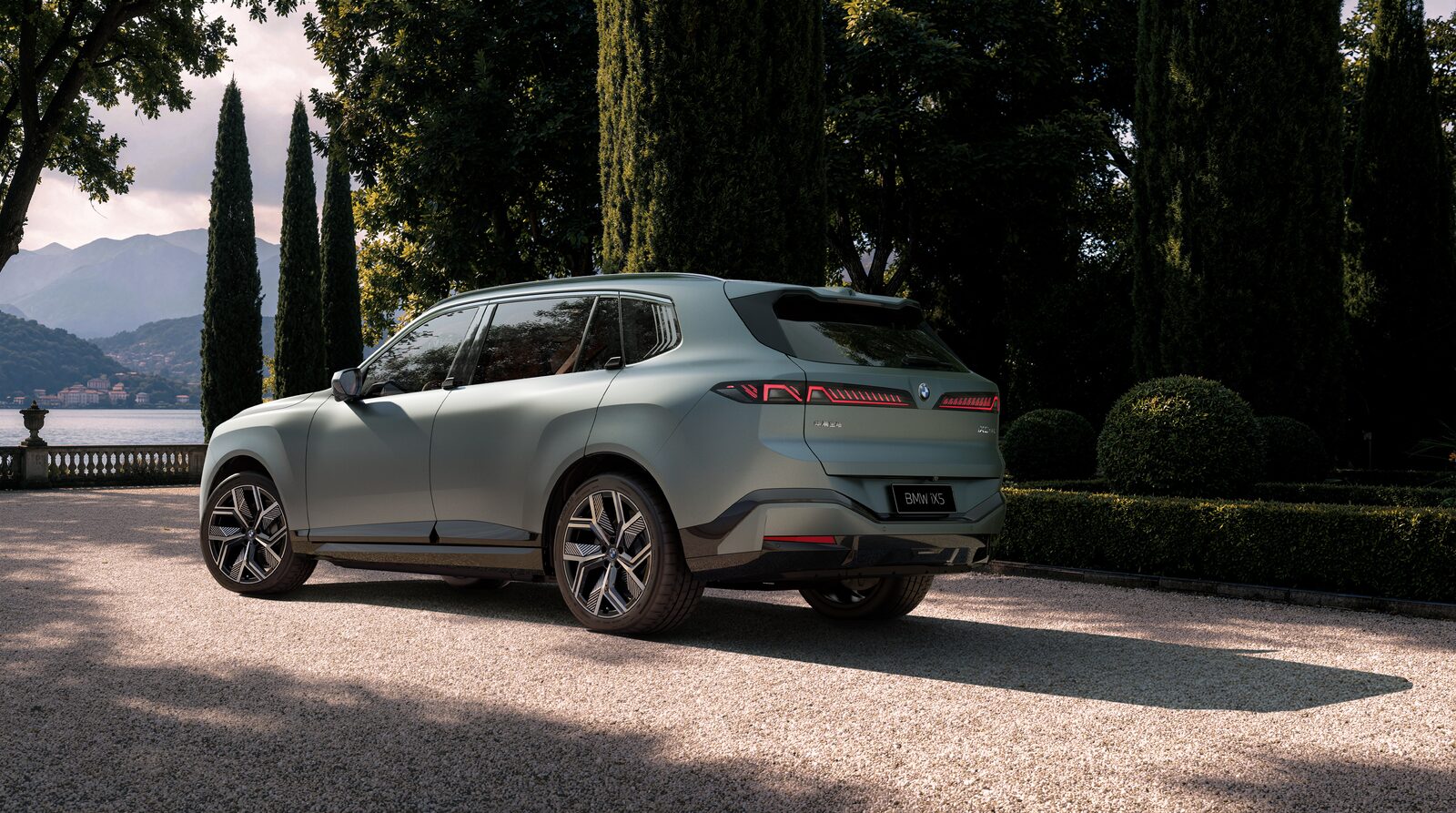 Ljusgrön BMW iX5 långaxlad snett bakifrån på en grusgång kantad av cypresser