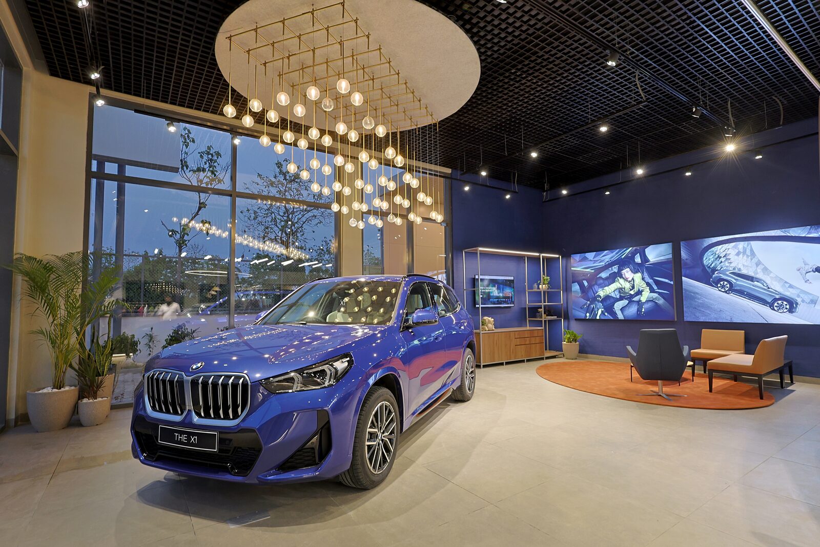 Blå BMW X1 i en modern BMW-bilhall med sittgrupp och stora skärmar på väggen