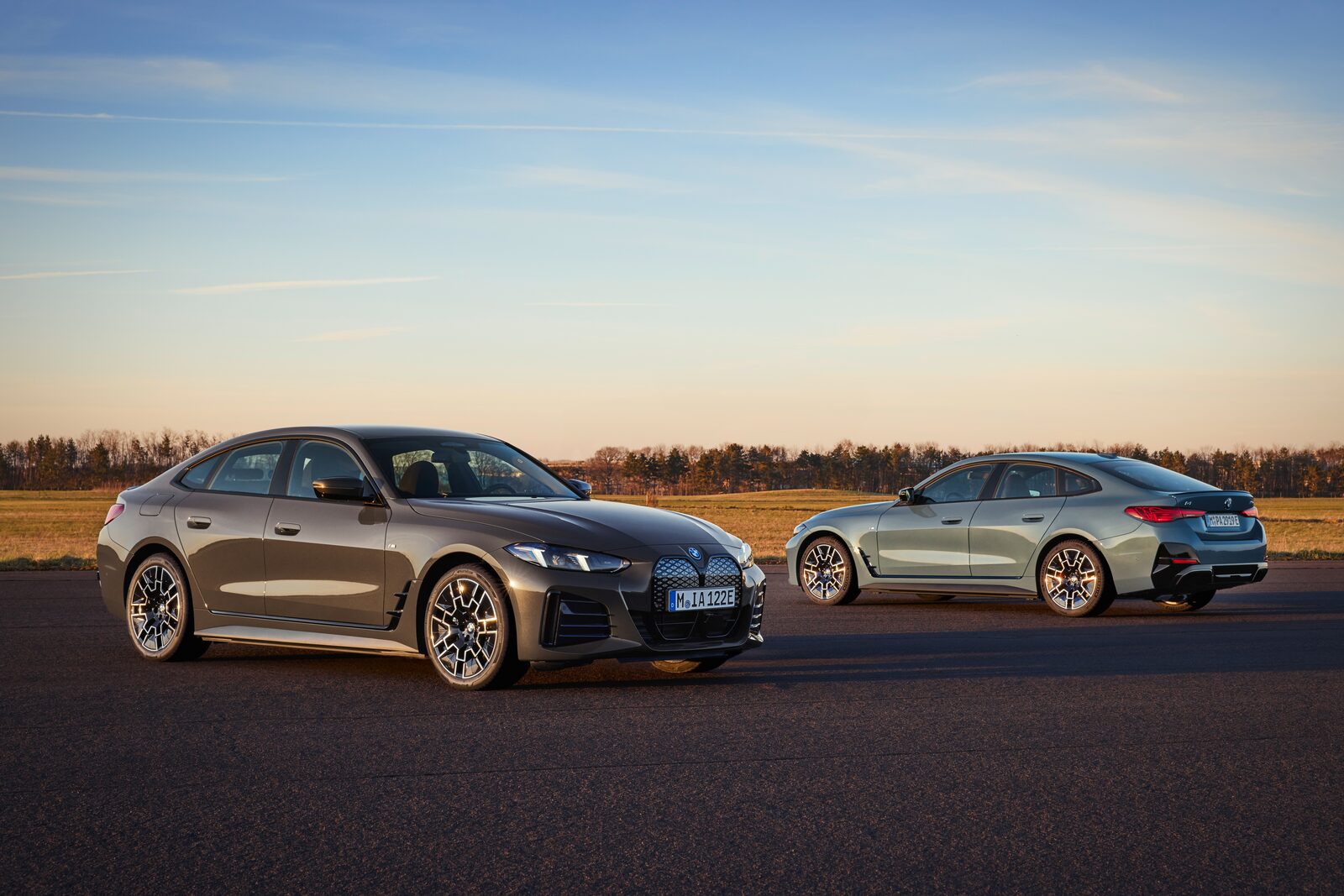 Två uppdaterade BMW i4 i brons och grågrönt parkerade på en landsväg i kvällsljus