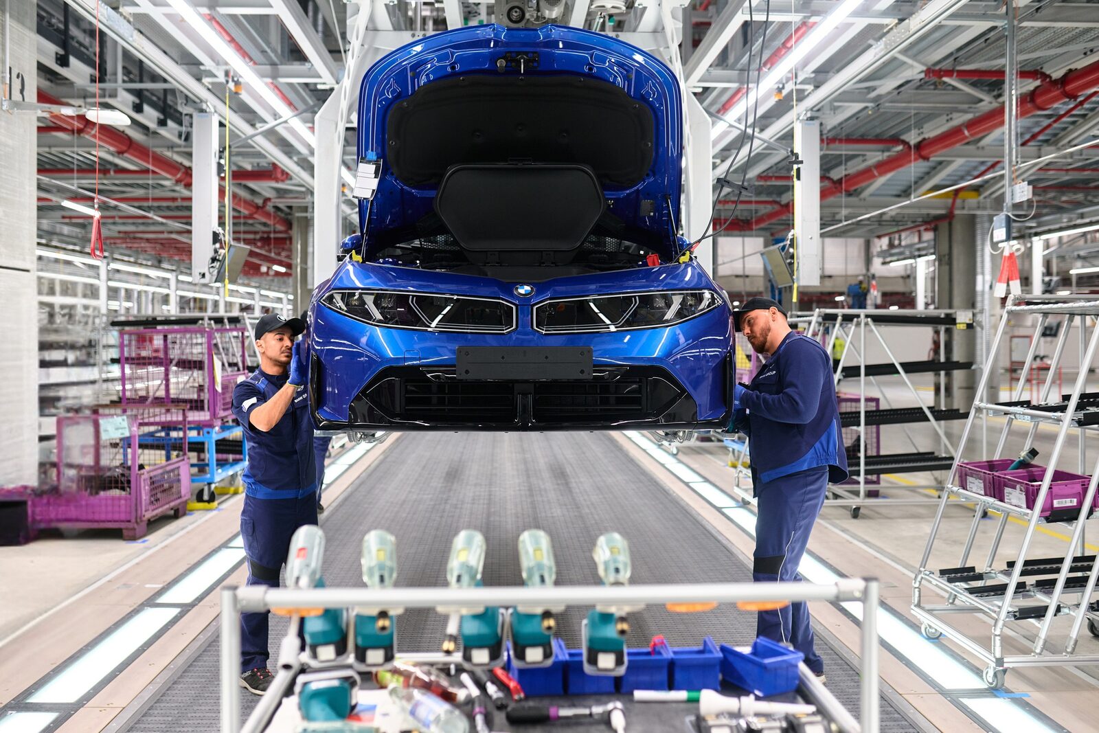 Två montörer i blå arbetskläder monterar fronten på en upphissad blå BMW i3 i fabriken