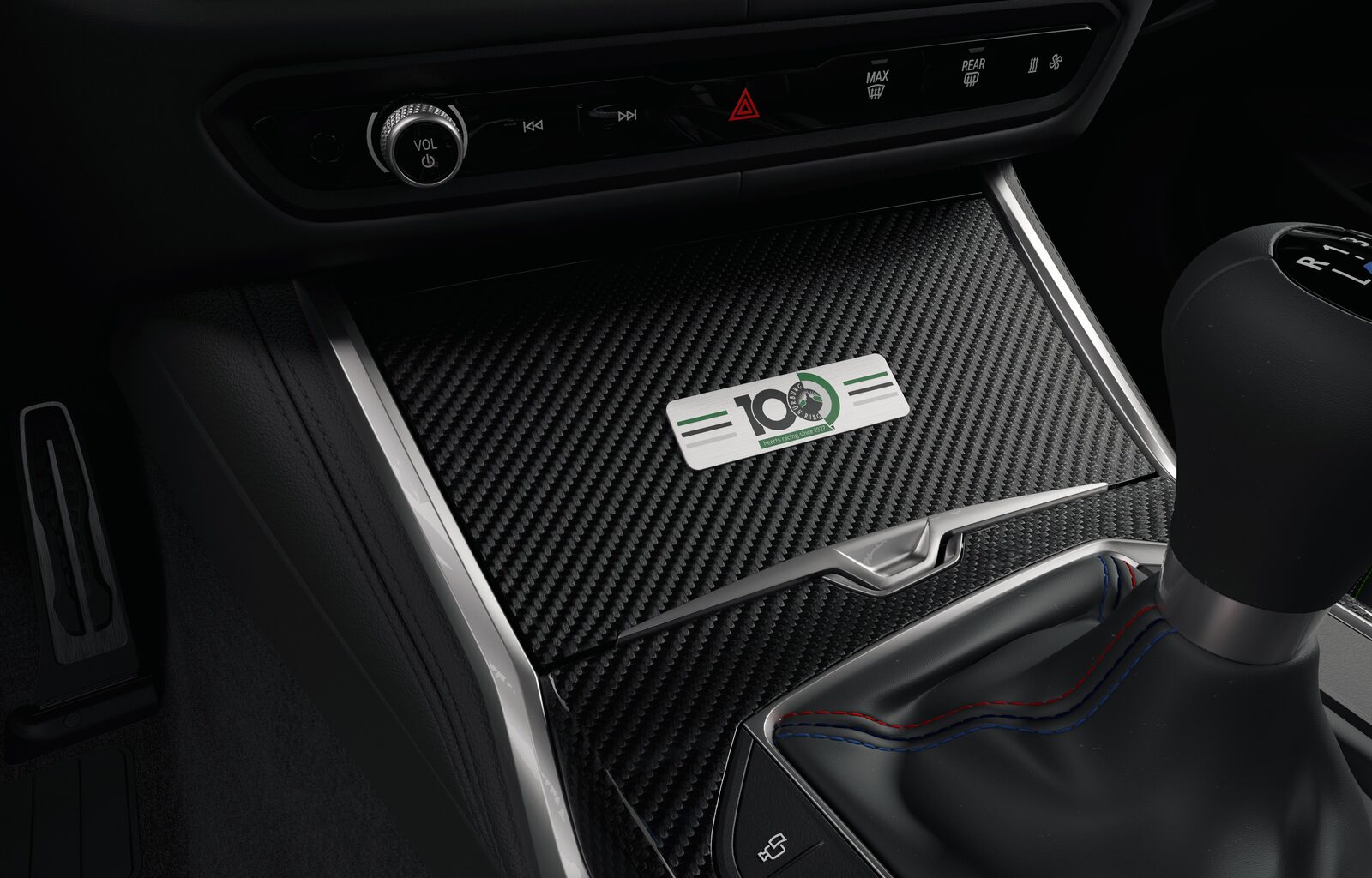 Detaljbild på kolfiberpanelen i mittkonsolen med jubileumsemblemet 100 Jahre Nürburgring i grönt och silver