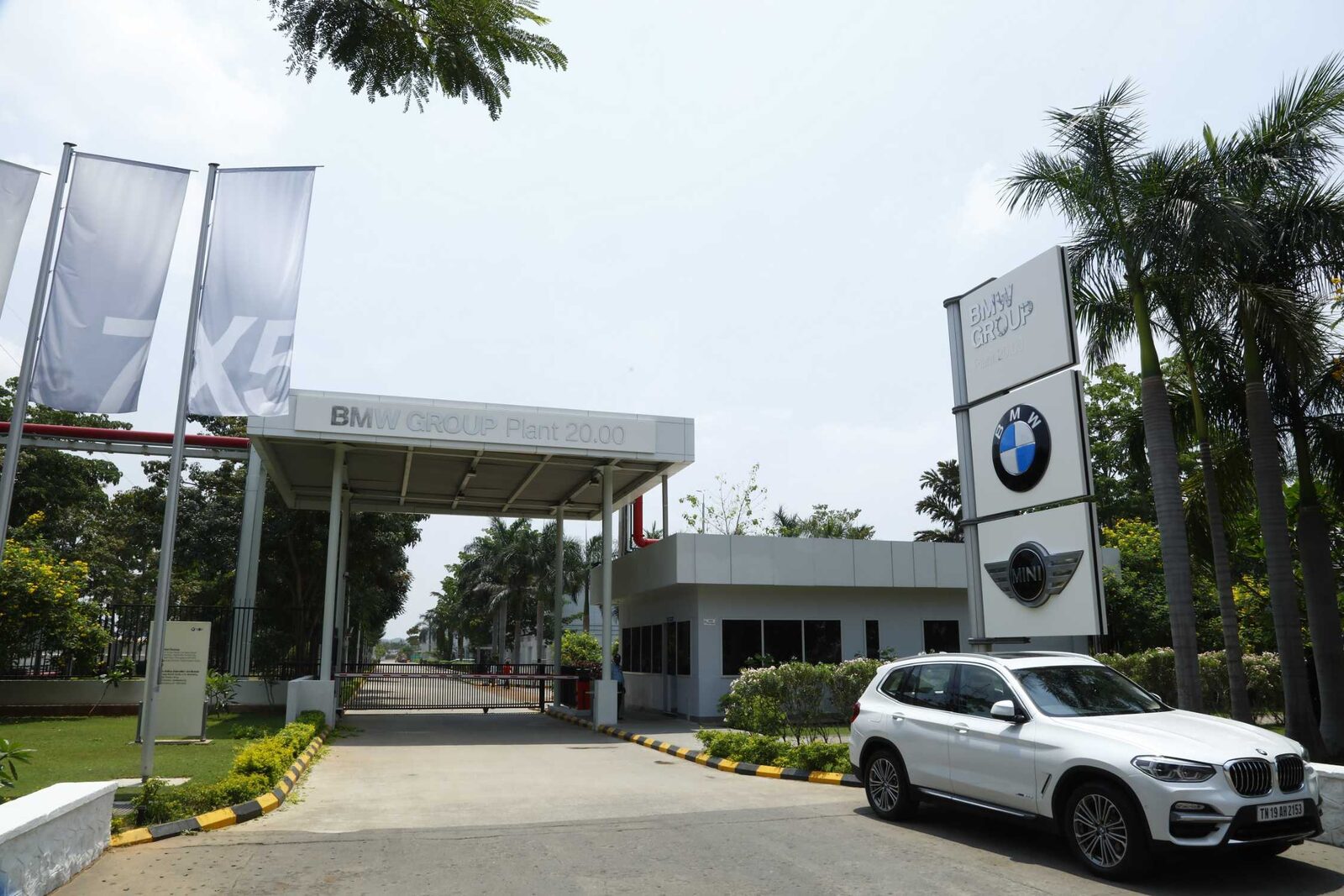 Infarten till BMW Group Plant Chennai med bom, skyltpylon med BMW- och MINI-logotyper, palmer och en vit BMW X3 parkerad till höger