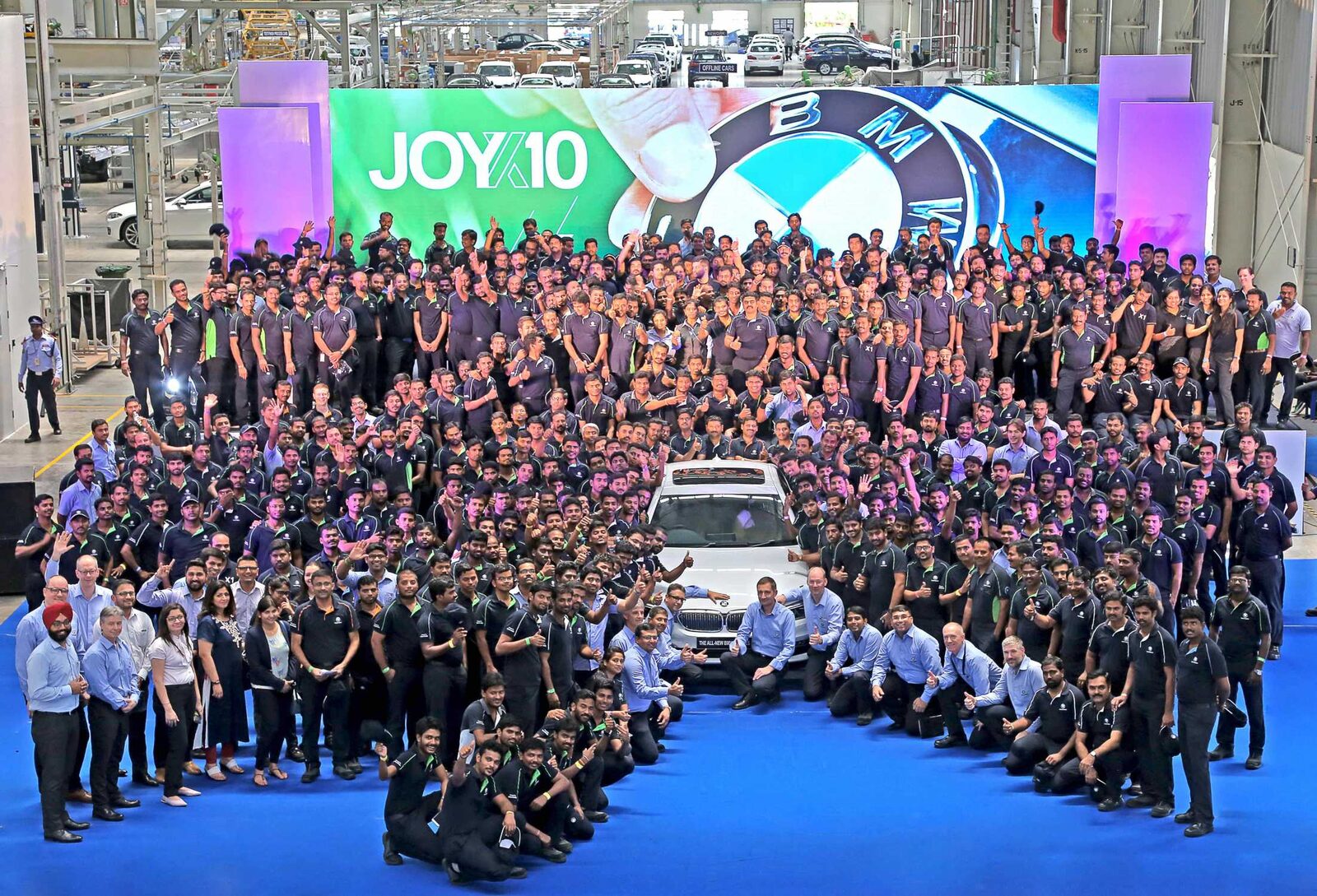 Flera hundra anställda vid BMW Plant Chennai samlade i monteringshallen kring en vit BMW framför en stor skärm med BMW-logotyp