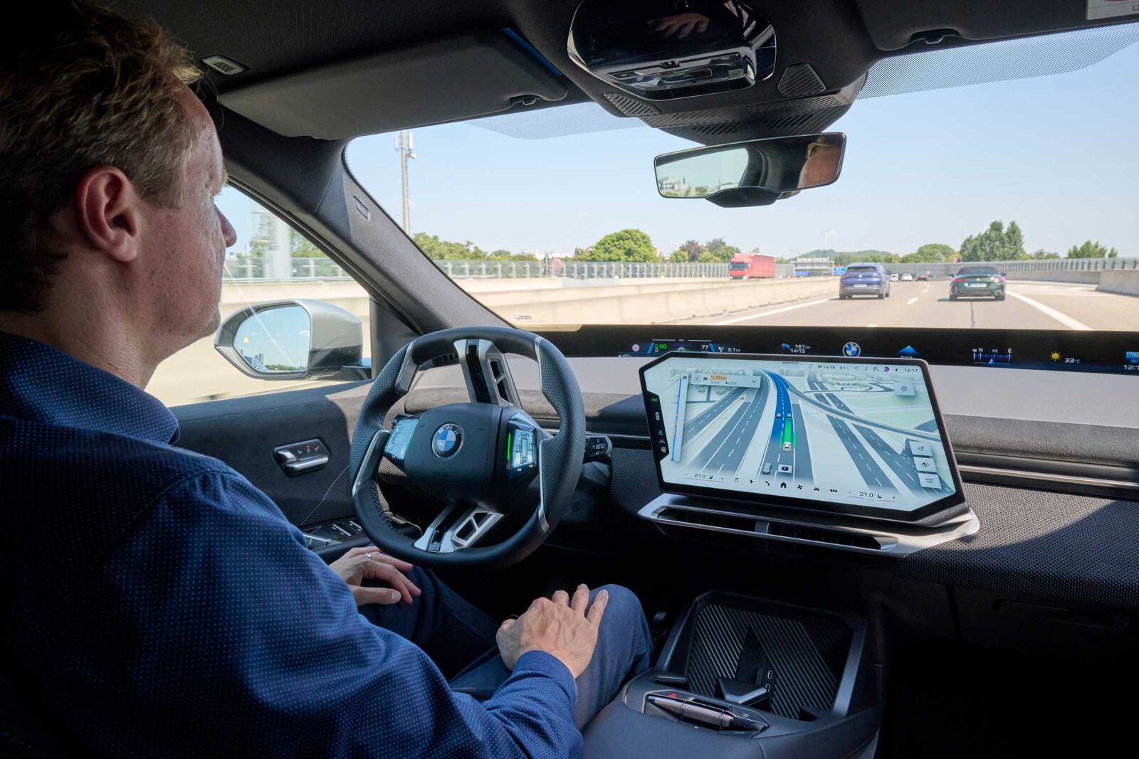 Förare med händerna i knäet medan bilen kör sig själv på motorvägen, mittskärmen visar en 3D-vy av en avfart med blå ruttlinje