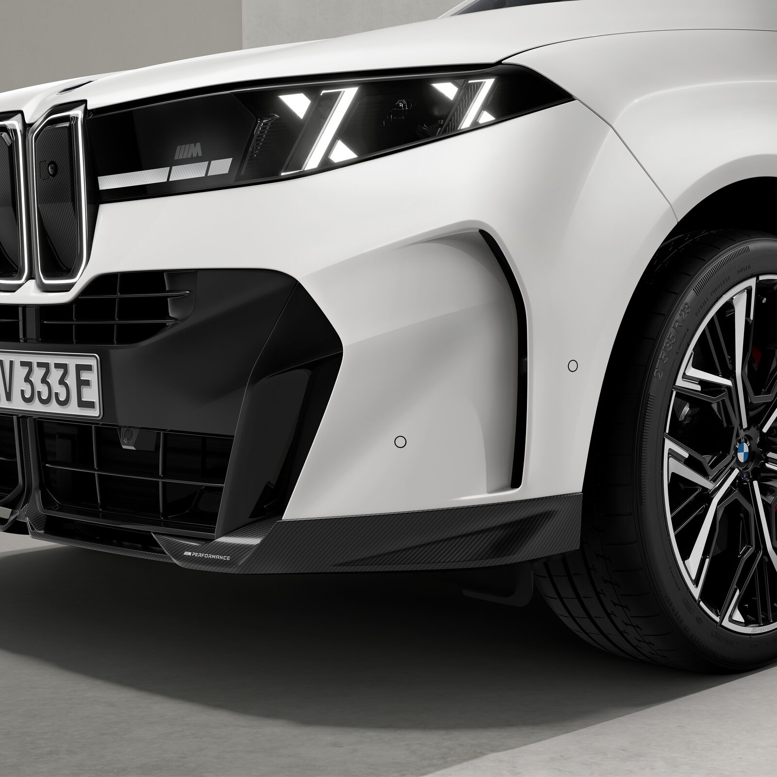 Vit BMW X5 snett framifrån i studio med svart M Performance-frontsplitter och svart sidoblad framför framhjulet