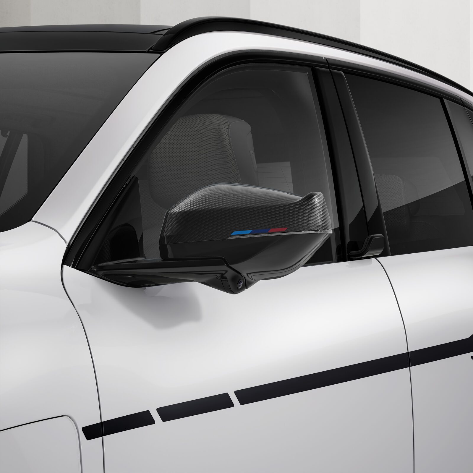 Närbild på mörk backspegelkåpa i aramid med M-färgad rand på en vit BMW X5, med svart M Performance-dekorrand längs dörren