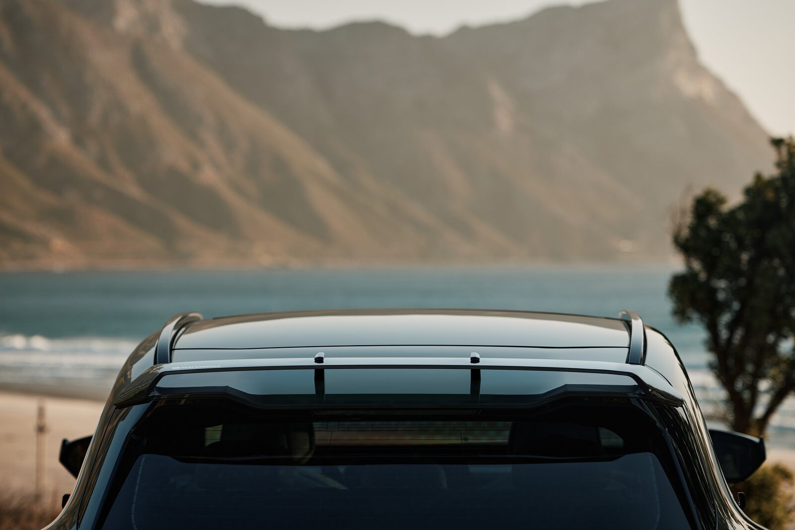 Närbild på BMW Aero-takboxen monterad på takrelingen med hav och berg i bakgrunden