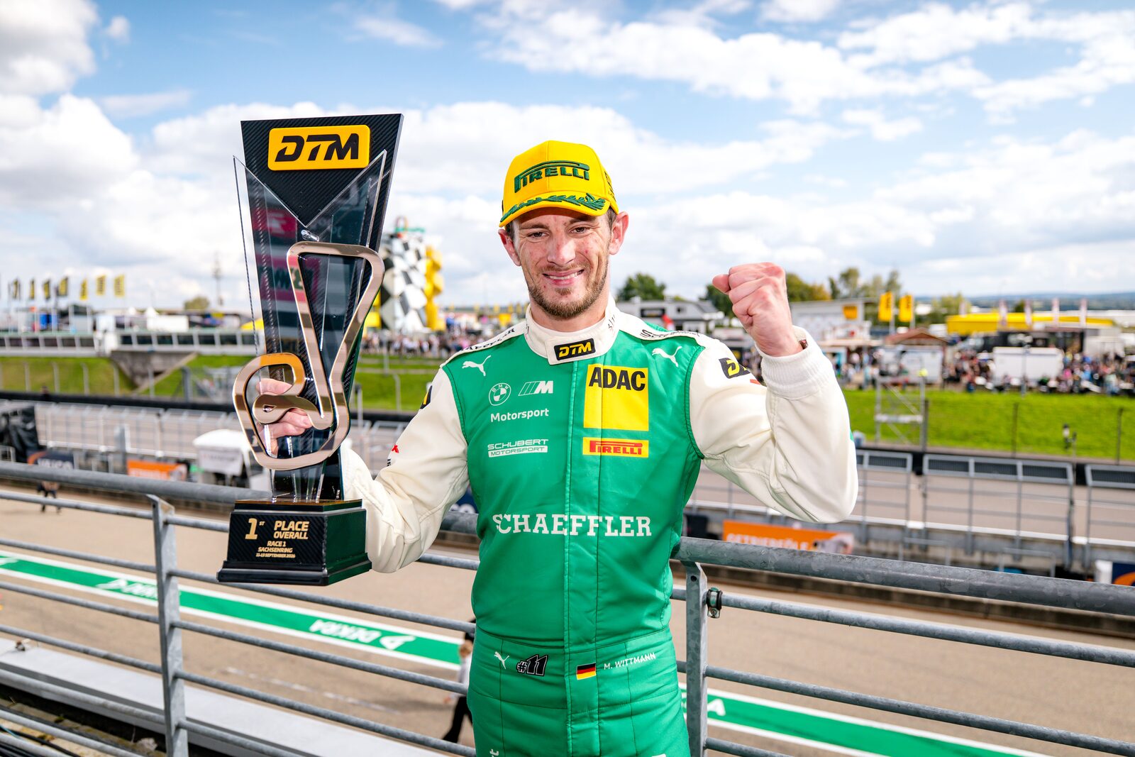 Marco Wittmann i grön tävlingsoverall håller upp segerpokalen från DTM med publiken bakom sig