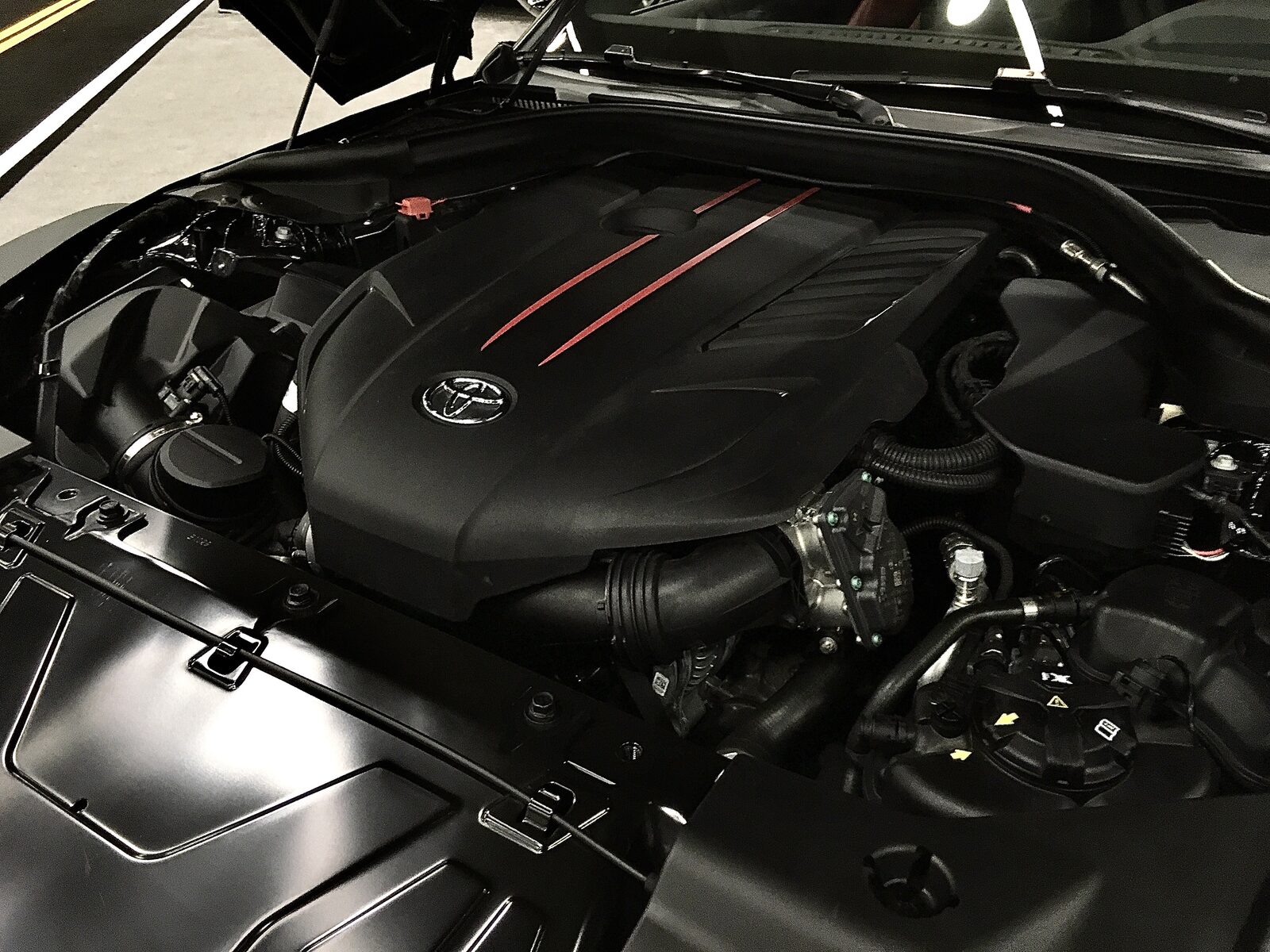 B58-motor med svart kåpa, Toyota-emblem och tre röda streck i motorrummet på en Toyota GR Supra