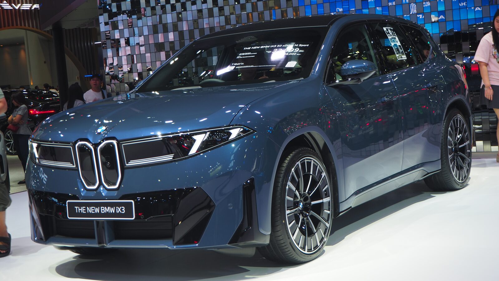 Grå BMW iX3 50 xDrive M Sport (Neue Klasse) fotograferad snett framifrån i en utställningshall