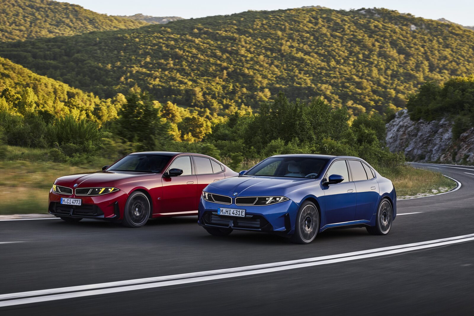 Röd BMW M350 xDrive och blå BMW i3 50 xDrive sida vid sida på en bergsväg