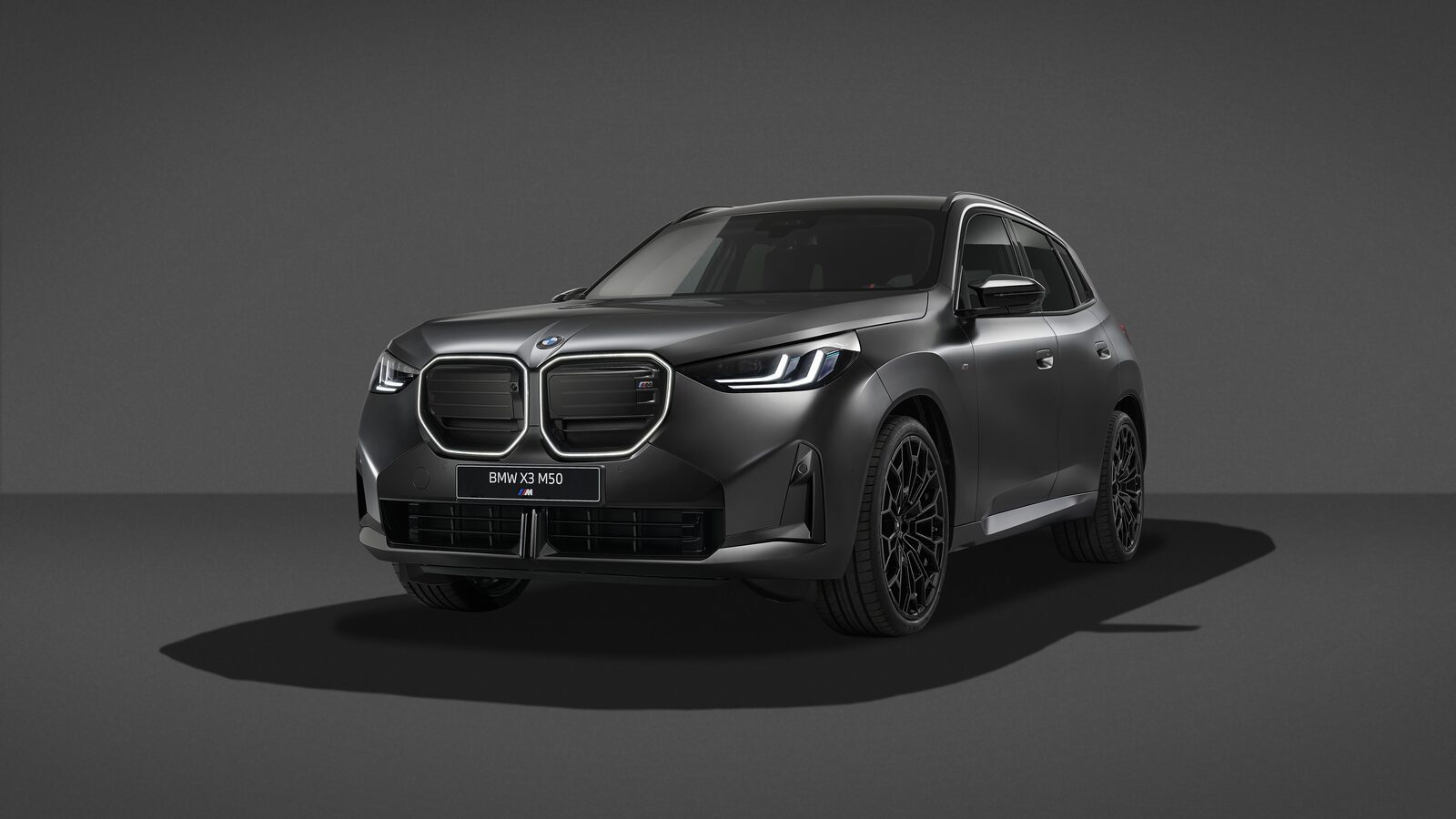 Mattgrå BMW X3 M50 xDrive med Black Package och svarta 22-tumsfälgar i en mörk studio