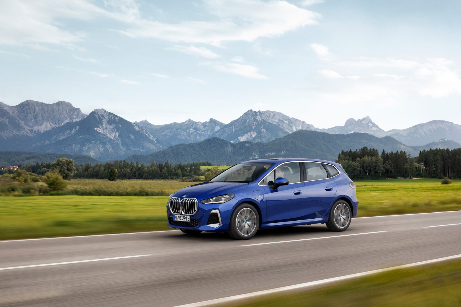 Blå BMW 2-serie Active Tourer i fart på en landsväg med alptoppar i bakgrunden