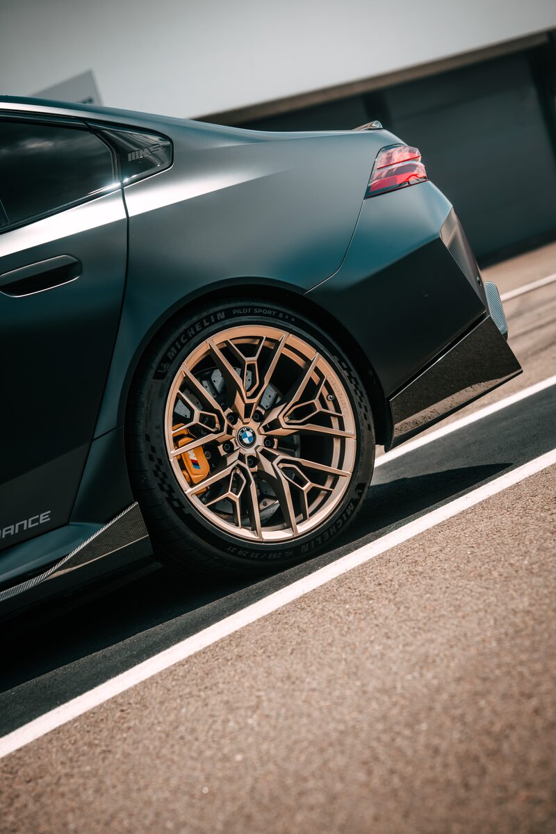 Bakre delen av en mörkgrå BMW M5 med Gold Bronze-fälg, fotograferad snett bakifrån på en bana
