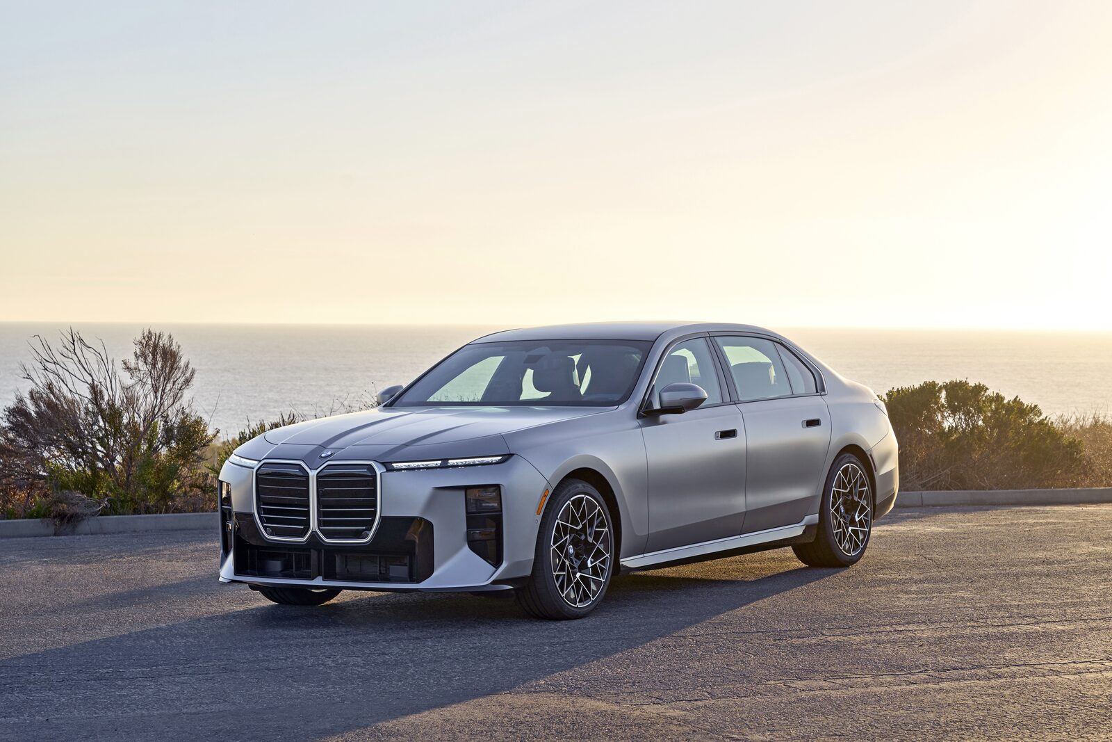 Silverfärgad BMW 7-serie med M Sport Pro-front och mörka njurar parkerad vid Stillahavskusten i solnedgång
